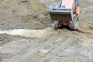 Heavy machinery operates on muddy construction site, shifting dirt preparing area for development.