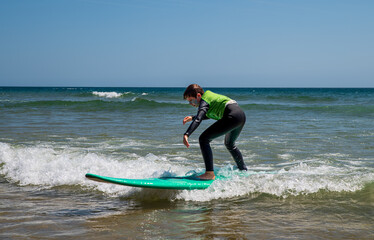 A 9-year-old boy wearing a wetsuit stands and slides on a surfboard, learning to surf in Portugal.
