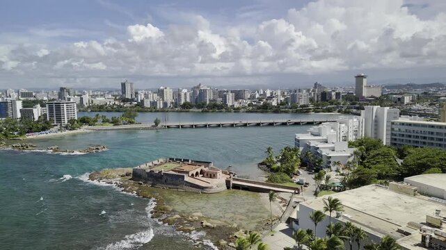 Drone orbits to the left around seaside fort at mouth of Laguna del Condado on sunny morning in San Juan, Puerto Rico