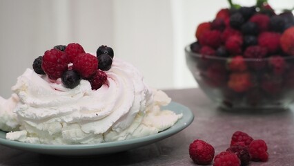 Meringues mini pavlova cakes with whipped cream decorated with fresh raspberries and blueberries berries and mint leaves on white marble background. Light summer dessert.