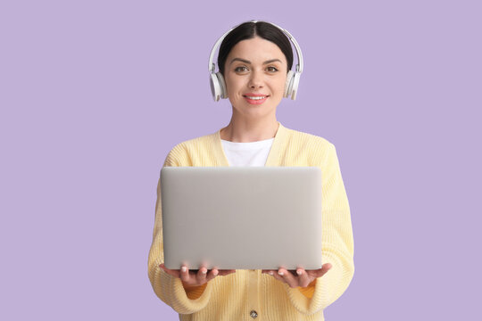Female programmer in headphones with laptop on lilac background