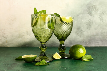 Glasses of tasty cold mojito on color table against light wall