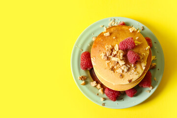 Plate of tasty pancakes with raspberries on yellow background