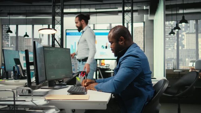 African american analyst writing growth strategy notes on a textbook, working in business office with insights and financial data. Consultant ensuring operational success and efficiency. Camera A. - Powered by Adobe