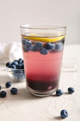 Glass of fresh blueberry lemonade and bowl with berries on white background