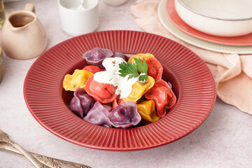 Plate of boiled colorful dumplings with sour cream and parsley on white background