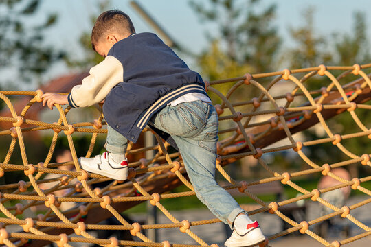 Little boy climbs in rope park or children playground at sunny day. Agility and climbing outdoor amusement center for children. Childhood and sport concept. High quality photo