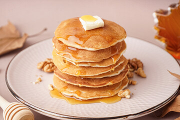 Plate of tasty pancakes with butter, nuts and maple syrup on beige background