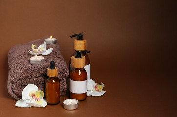 Bottles of cosmetic products, clean towel and burning candles on color background