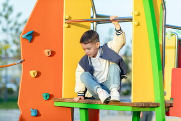 Little boy climbs in rope park or children playground at sunny day. Agility and climbing outdoor amusement center for children. Childhood and sport concept. High quality photo