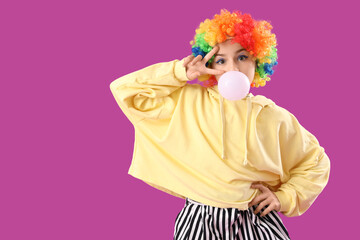 Trendy girl in clown costume blowing bubble gum on purple background