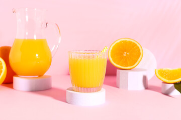 Decorative podiums with glass and jug of fresh orange juice on pink background