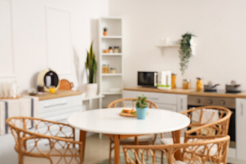 Blurred view of light kitchen with green plants, counters and dining table