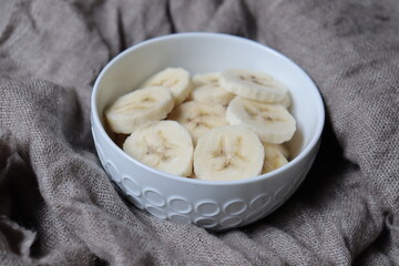 Banana slices in a white bowl with a natural background. Healthy and natural snack and fruit salad. Desert with fruits.