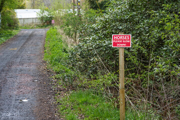 Horses Please Slow Down red and white warning sign on wooden post on country lane