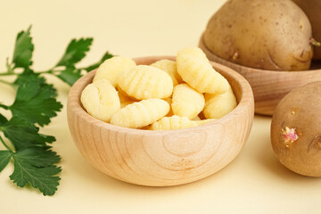 Wooden bowl with tasty gnocchi and parsley on beige background, closeup