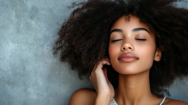 African woman with curly hair in white tank top, posing against concrete wall