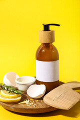 Composition with bottle of cosmetic product, natural ingredients and hair comb on yellow background