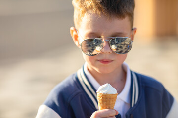 Child boy in fashion sunglasses and summer clothes eats ice cream on a hot day in park. Ice cream...