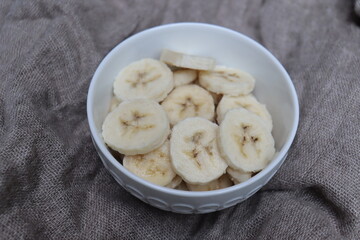 Banana slices in a white bowl with a natural background. Healthy and natural snack and fruit salad. Desert with fruits.