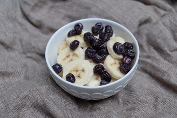 Blueberries and bananas in a white bowl and with natural background. Healthy and natural snack and fruit salad. Desert with fruits.