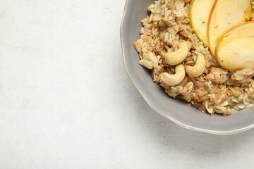 Tasty oatmeal with apple and nuts in bowl on white background, closeup