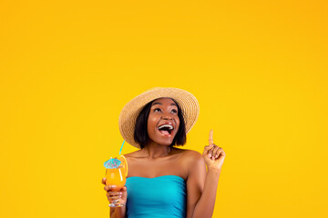 Millennial black lady with yummy tropical cocktail screaming WOW and pointing upwards on orange studio background. Excited African American woman advertising summer sale or promo