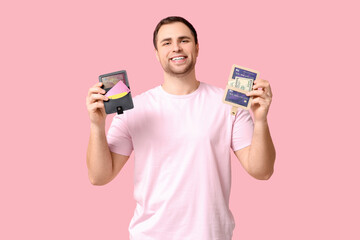 Young man holding wallets and credit cards on pink background