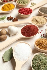 Different aromatic spices in spoons on white wooden table, closeup