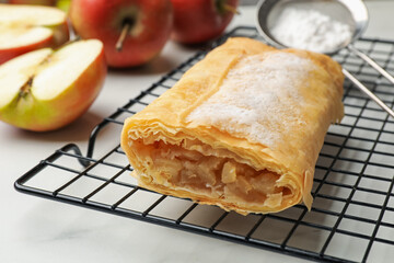 Tasty apple strudel with powdered sugar and fruits on white marble table, closeup
