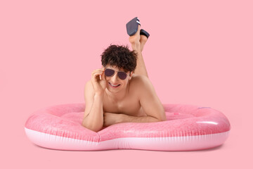Handsome young happy man with inflatable mattress in shape of heart lying on pink background