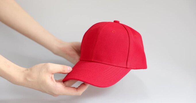 Woman presenting red baseball cap on grey background, closeup