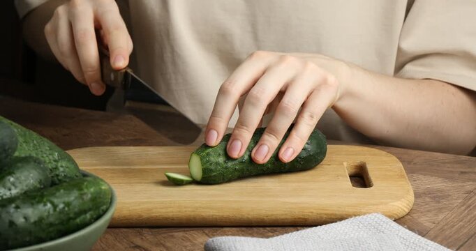 Woman cutting fresh cucumber at wooden table, closeup