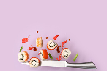 Tasty flying sushi rolls, ginger, sauce and knife on lilac background