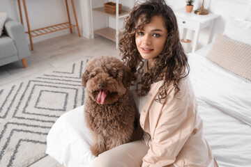 Young woman with funny poodle sitting in bedroom