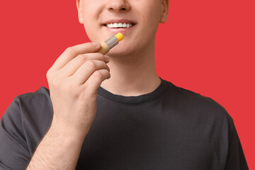 Young man with lip balm on red background, closeup
