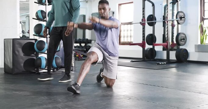 African American trainer guiding client through kneeling stretch and lunges in gym for mobility