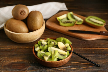 Bowls and board with fresh kiwi on wooden background
