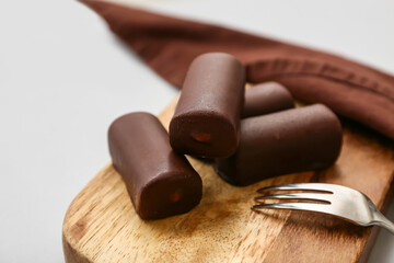 Wooden board with tasty chocolate glazed curd snacks with vanilla flavor on light background, closeup