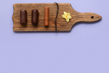 Wooden board with tasty chocolate glazed curd snacks with vanilla flavor on lilac background