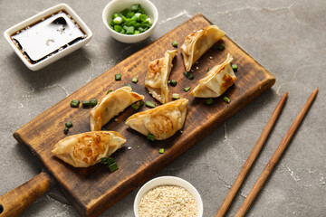 Wooden board with fried Japanese gyoza and bowl of soy sauce on grey background