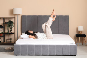 Happy young African-American woman with pillow lying on soft mattress in bedroom