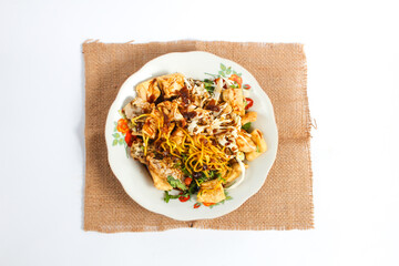 Solo Kupat Tofu on a rattan handkerchief isolated on a white background. Made from yellow noodles, fried tofu, fried peanuts, fried fritters, cabbage, ketupat and sweet peanut sauce
