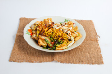 Solo Kupat Tofu on a rattan handkerchief isolated on a white background. Made from yellow noodles, fried tofu, fried peanuts, fried fritters, cabbage, ketupat and sweet peanut sauce