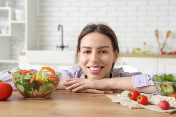 Beautiful young woman with glass bowls of fresh vegetable salad at table in kitchen