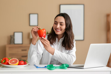 Young female nutritionist with bell pepper at table in office