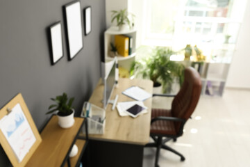 Interior of office with workplace, armchair, modern computer, houseplant and shelving unit near black wall, blurred view