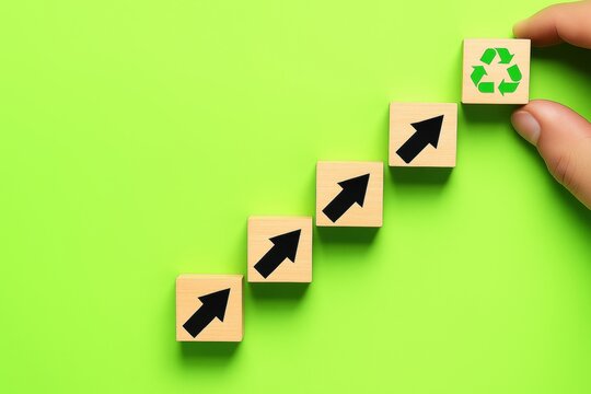 Environmental Growth: A hand strategically positions a recycling symbol block atop a series of arrow-marked blocks, illustrating the upward trajectory of environmental consciousness and progress.