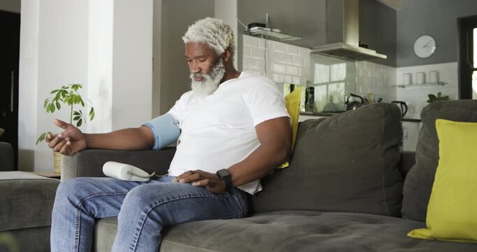 Pressing start, African American man measuring BP by inflating cuff at home and reading results