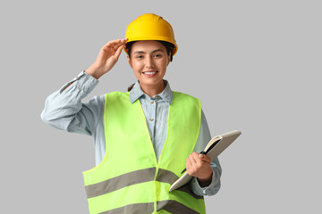 Fototapeta premium Young female construction worker with notebook and pen on grey background. Woman in male profession concept